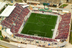 Um dos principais lugares para apreciar os esportes em Toronto: o estádio BMO Field, em Toronto, durante partida do time Toronto FC, da Major League Soccer. As arquibancadas estão completamente lotadas por torcedores vestidos majoritariamente de tons vermelhos enquanto a partida acontece no centro do gramado
