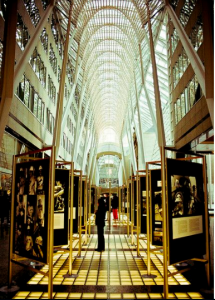 A imagem mostra uma das saídas do PATH para a Eaton Centre, a maior rede de lojas canadense. O túnel de teto de vidro mostra um corredor repleto de fotografias, em uma espécie de exposição artística. Uma pessoa, no centro da imagem, observa pacientemente uma das fotografias expostas
