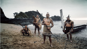 A imagem exibe quatro guerreiros maoris recém-chegados a uma praia, por meio de uma canoa longa. O dia está nublado e os nativos, todos armados, não apresentam expressões muito amigáveis. Três deles são adultos, com exceção ao guerreiro agachado à esquerda. Os adultos apresentam tatuagem no dorso, e todos possuem roupas típicas.
