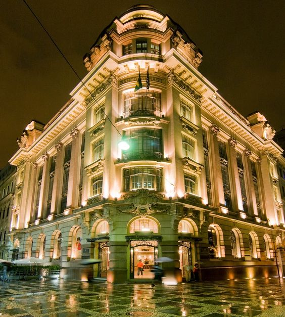 Descrição da imagem: a foto mostra o CCBB à noite, com todas as suas luzes acesas. O imponente edifício fica bem em uma esquina, o que explica o estilo arquitetônico clássico.