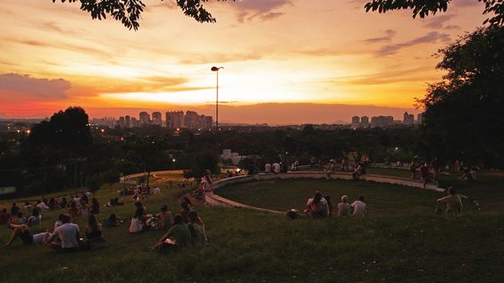 Descrição da imagem: A imagem mostra a Praça do Pôr do Sol com muitas pessoas sentadas na grama e nas muretas presentes no local. No céu, um bonito espetáculo laranja entretém os espectadores.