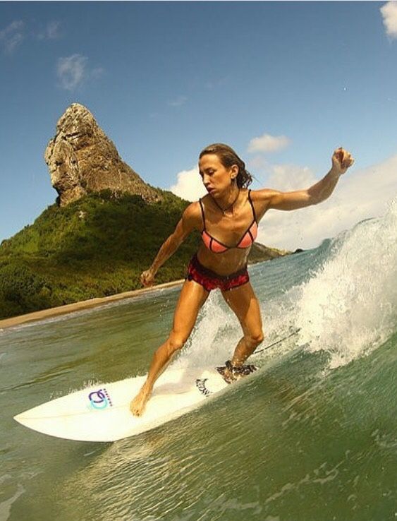  Descrição da imagem: A foto mostra uma moça pegando uma onda com a sua prancha em uma das praias de Fernando de Noronha.